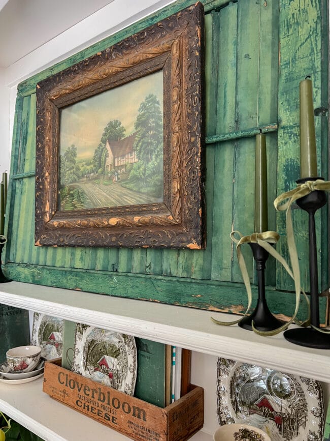 vintage green shutter with an old print and candle sticks sitting on a hutch shelf