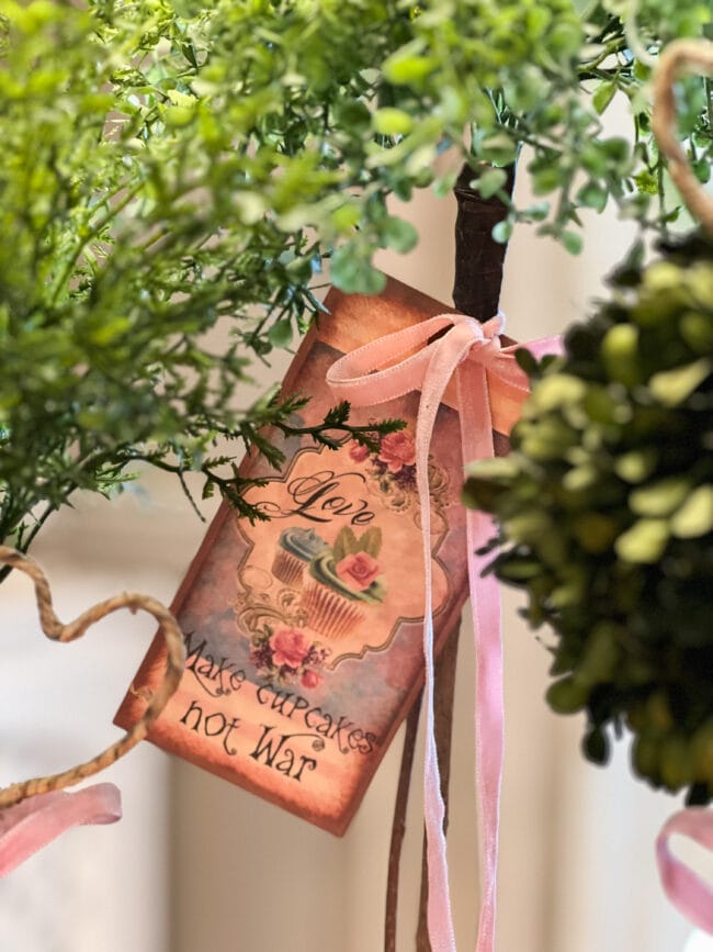 close up of a vintage looking valentine tied with ribbon to the stem of a topiary