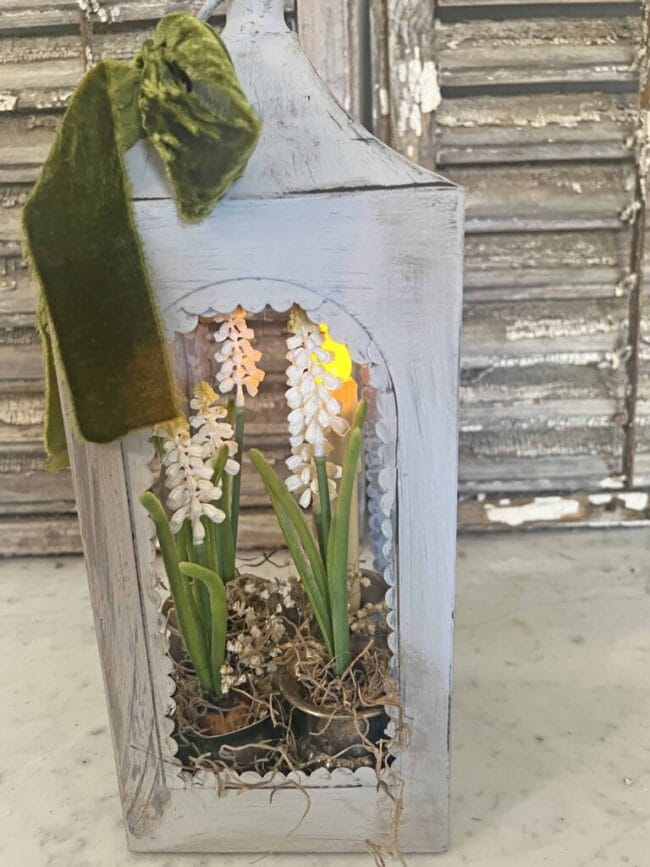 gray metal lantern with flowers inside and a green velvet bow
