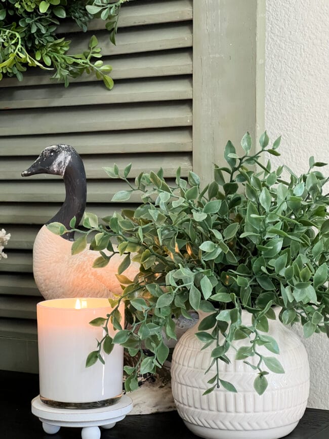 white candle, white pottery with faux plant and a goose