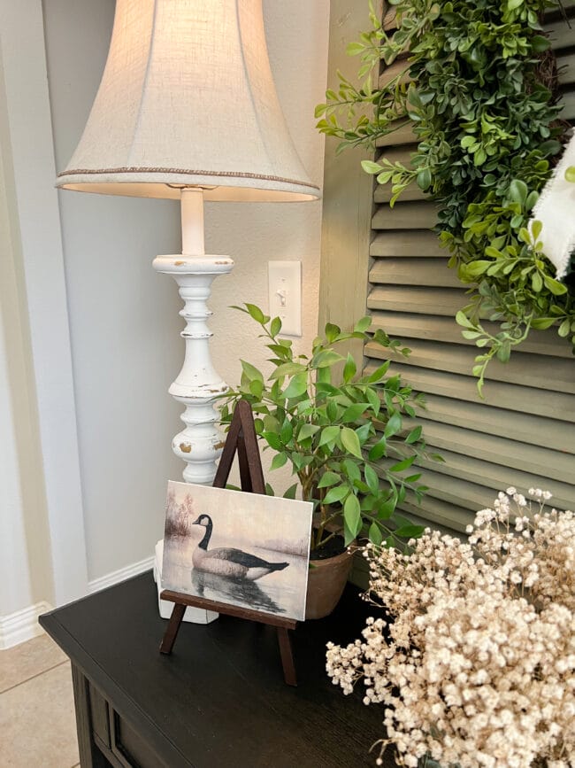 lamp, small goose painting on a tabletop easel with plants