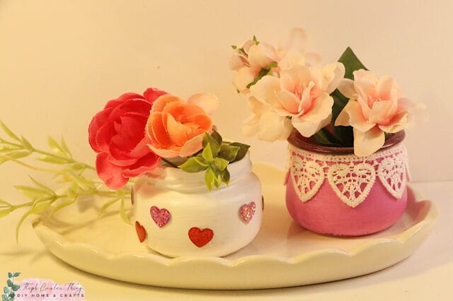 two small jars with flowers and decorated for valentines day. 