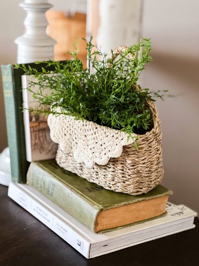 small basket with faux greenery and a doily sitting on top of green books
