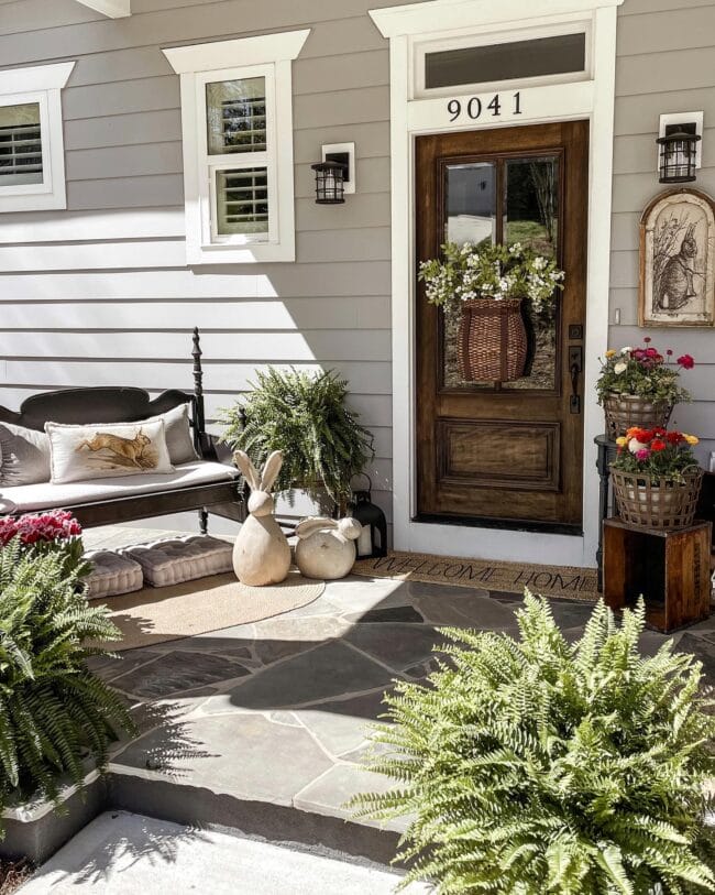 porch with bench, ferns, basket on door and concrete bunnies 