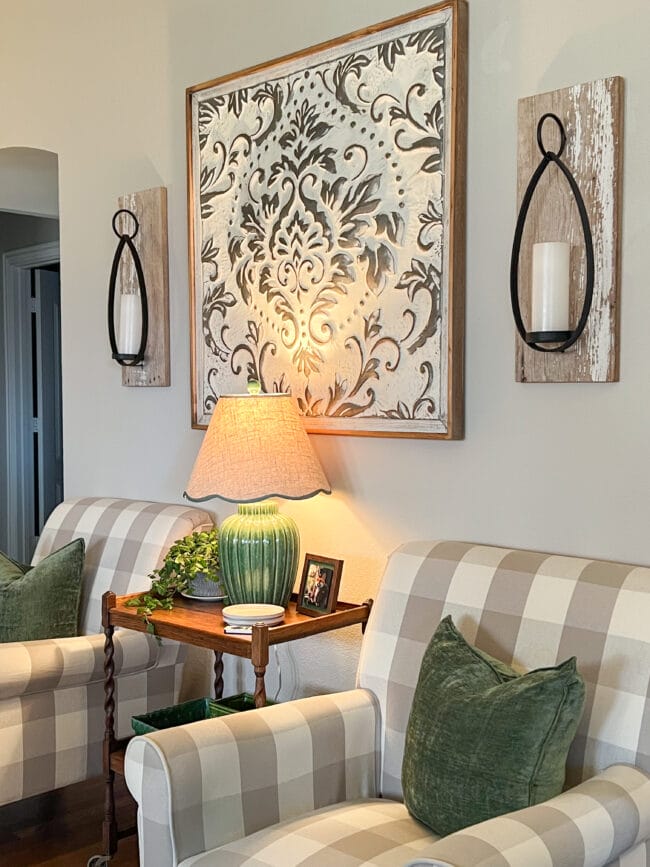 checked chairs with a green lamp, green pillows and a large metal piece on the wall with candle scones on either side