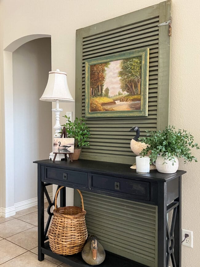vintage green screen door behind black console table with ducks, a painting and faux plants
