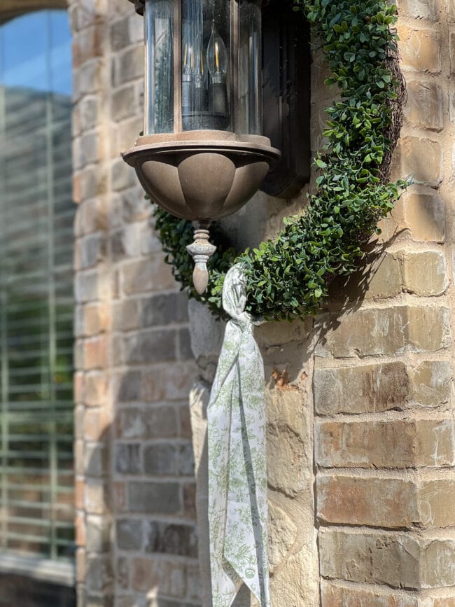 green and white sash tied around a boxwood wreath hanging over an outdoor light fixture