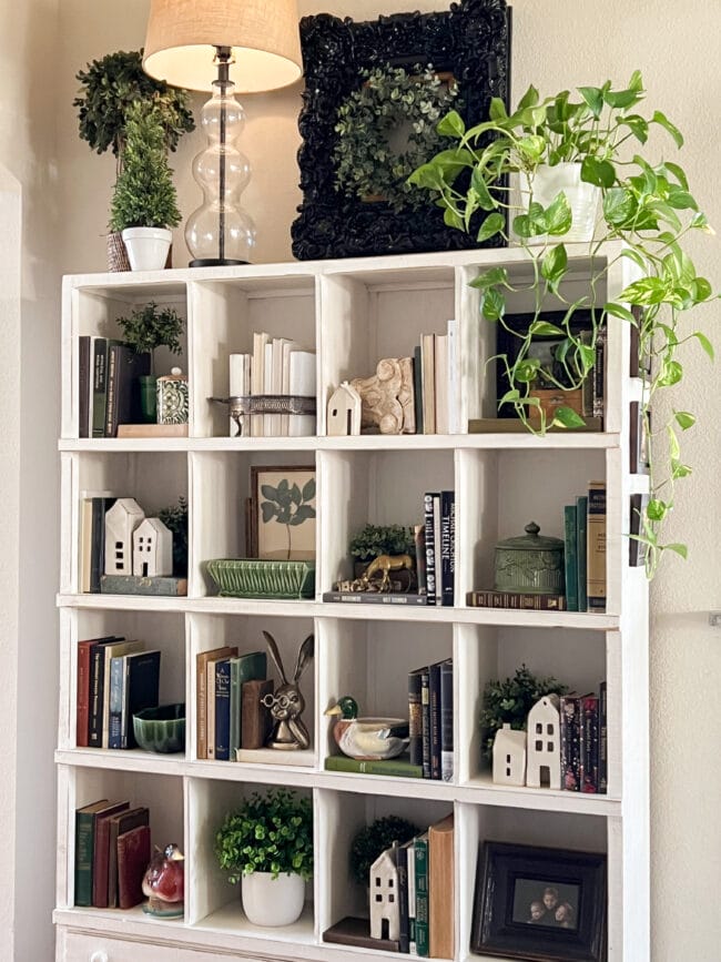 bookcase with green plants, books, white candles and houses and an overall spring look