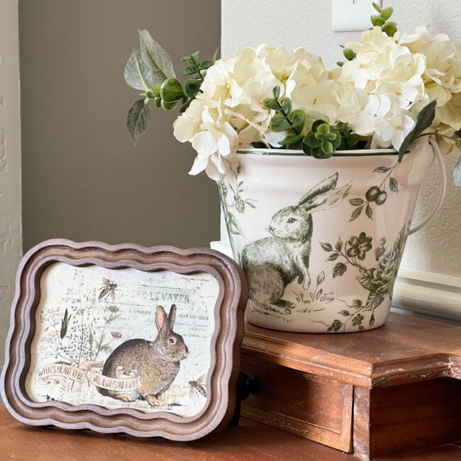 framed bunnie postcard and a green white bunny bucket with faux hydrangea stems inside