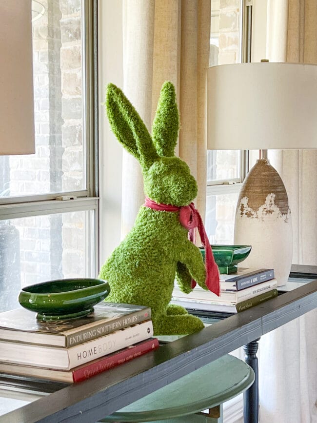 console table with tall green bunny, coffee table books, lamps and green pottery