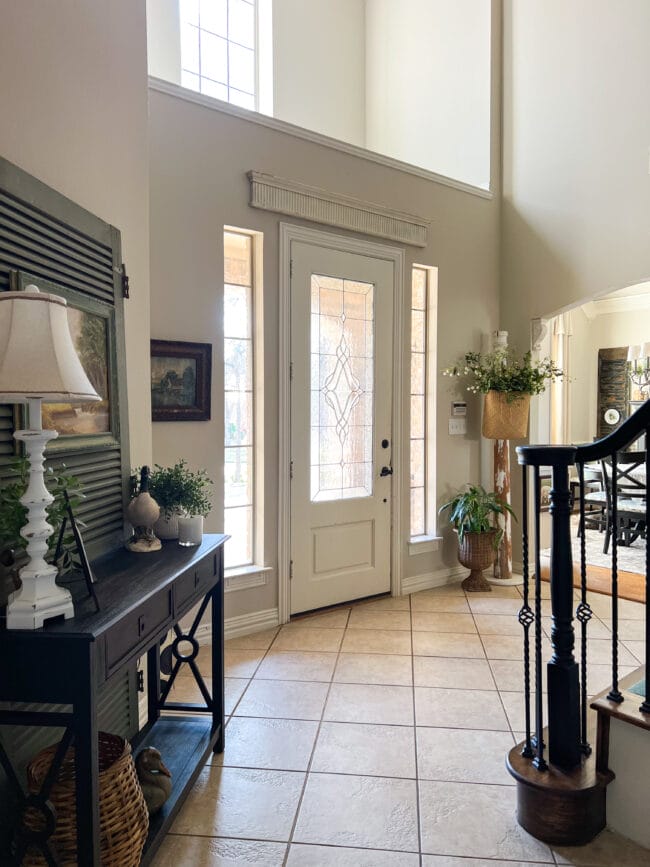 entry with black console table, lamp, vintage screen door and different home decor pieces with faux plants
