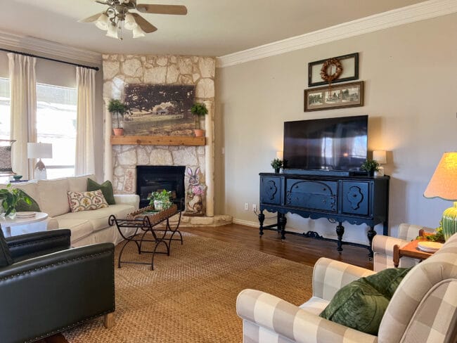 living room with black sideboard with TV on it, stone mantel with columns and farmhouse print. 