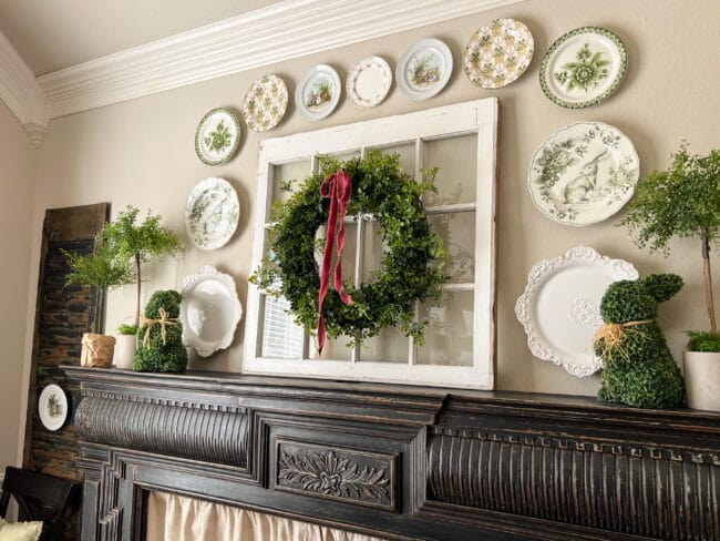 close up of black mantel with spring plates, a vintage window with a wreath hanging on it