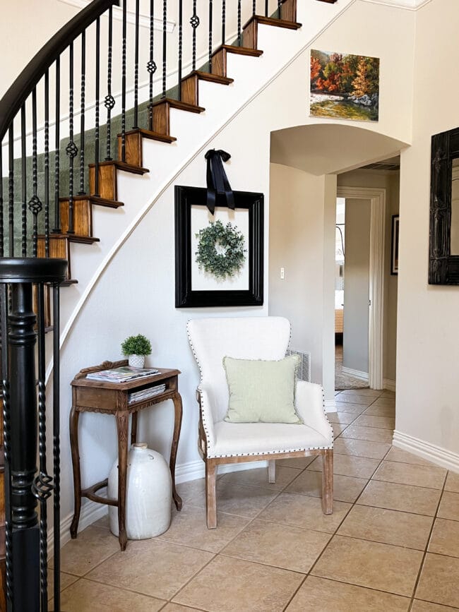 entryway with curved stairs, chair with a pillow, frame with a wreath and a side table