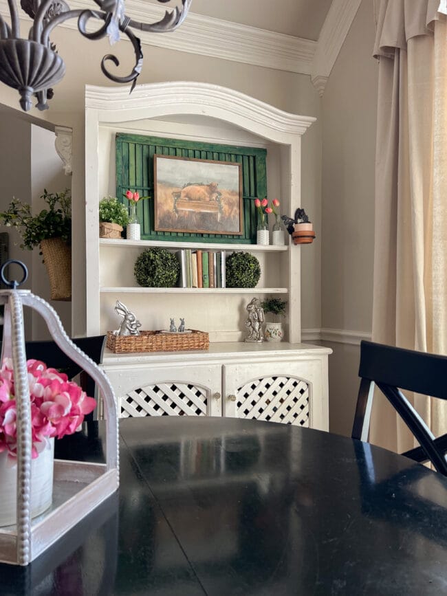 white vintage hutch with green shutter, cow print, pink tulips and faux greens on the shelves