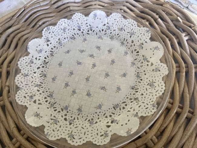 wicker placemat with a clear plate and a doily with lavender flowers underneath