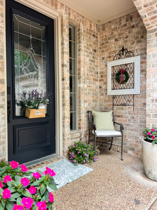 brick house porch with an iron chair, plants and burlap box hanging on black front door
