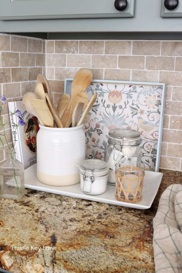Floral papered tray sitting behind a white utensil jar, sugar jar and a candle in the kitchen