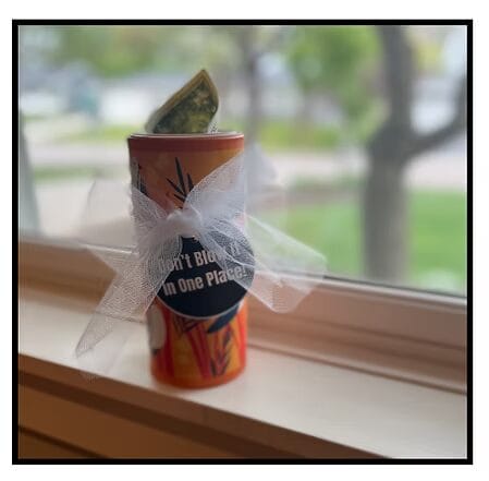 a kleenex box with money coming out of the top and a white ribbon around it.