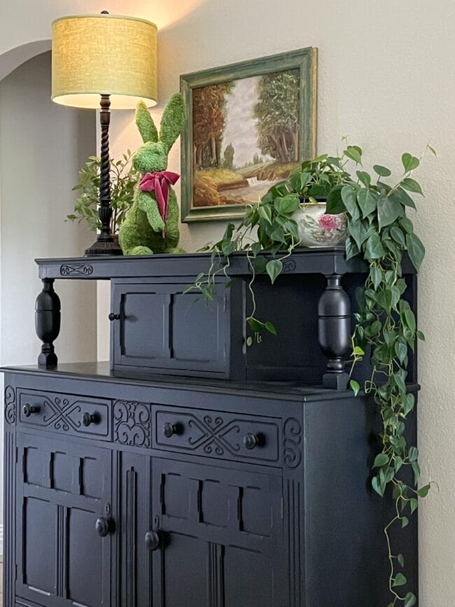 black cabinet with plant, lamp, painting and fuzzy bunny statue