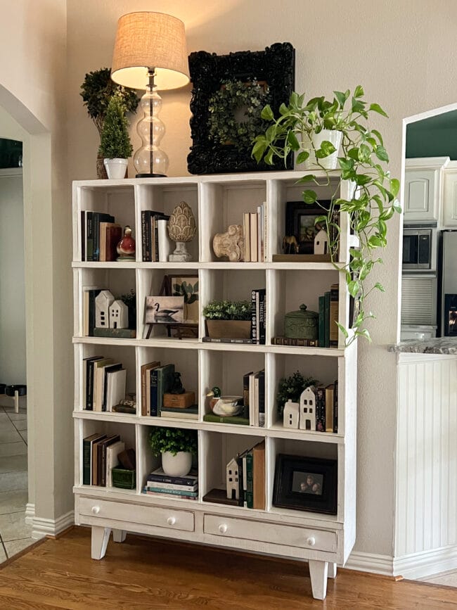 cubby shelf with books, plants, lamp on top with a black frame and wreath
