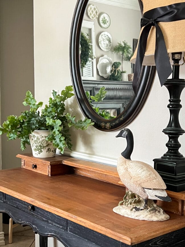 desk with black mirror, lamp, goose statue and a plant inside an ice bucket