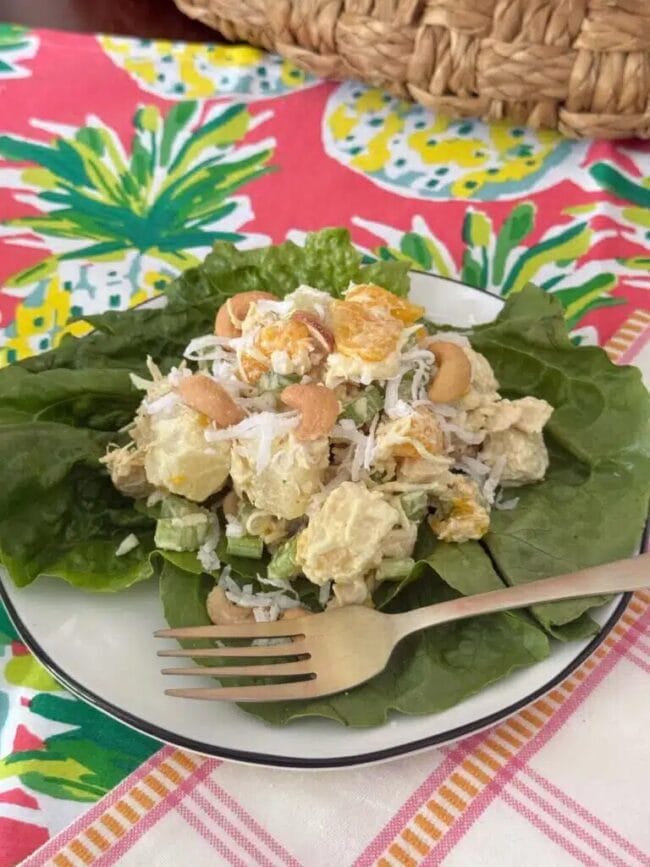 tropical summer curry salad on a bed of lettuce with a bright tablecloth underneath the plate