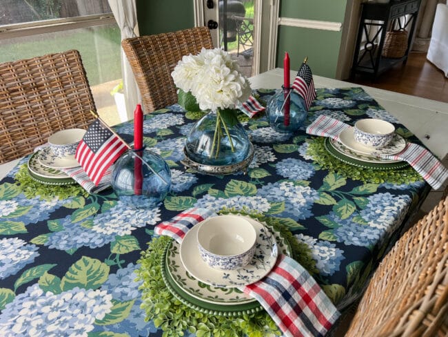 blue and green tablecloth with blue glass vases, red candles and white flowers with flags.