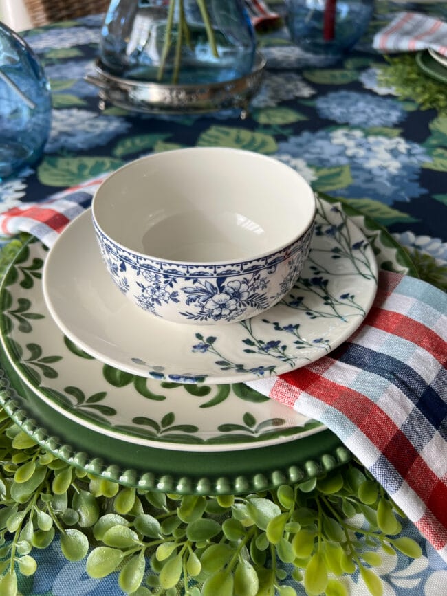 place setting with a boxwood placemat, green and white plates, a blue and white bowl and a red, white and blue cloth napkin in the middle