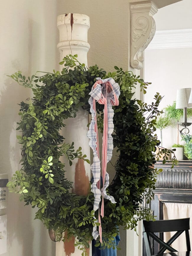 boxwood wreath hanging on vintage column with red, white, and blue bows