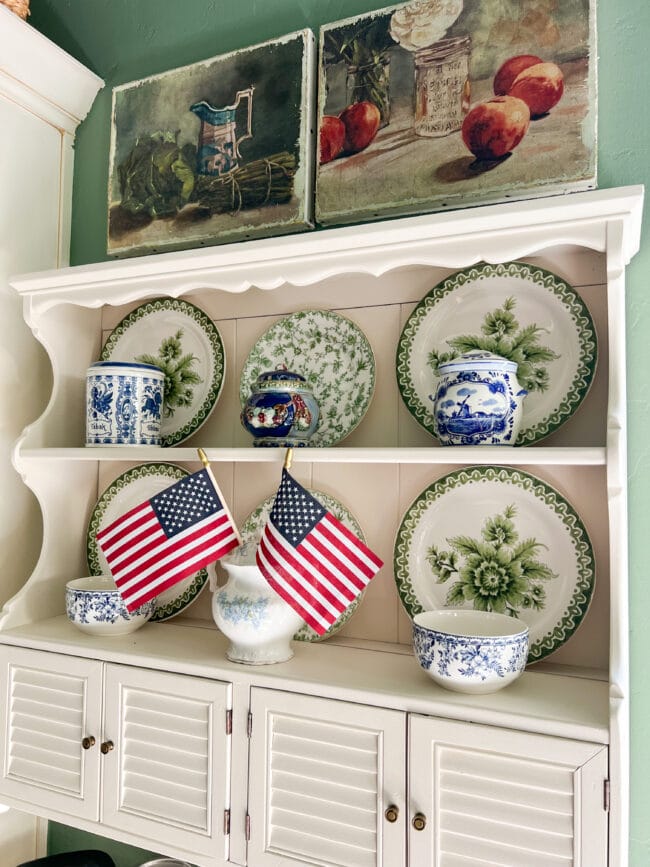 Hung white shelf with green plates and blue and white china pieces and two small US flags