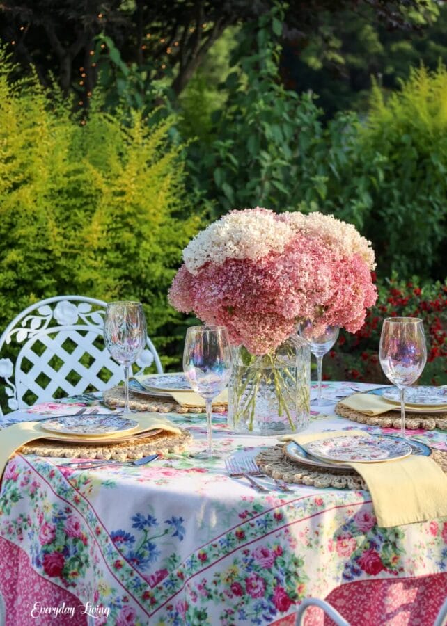 outdoor tablescape with dual tablecloths, pink and white flowers, and plates with pinks, blues, and green accents
