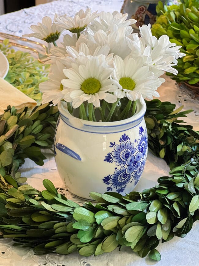 blue and white jar with daisies and a green wreath around it