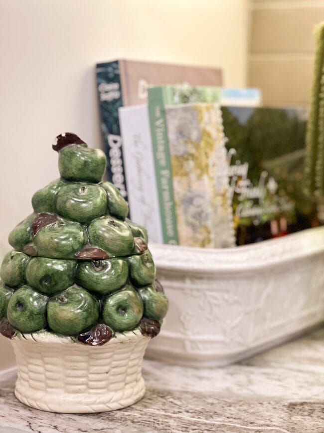 green apple canister and cookbooks stacked in a white vintage planter