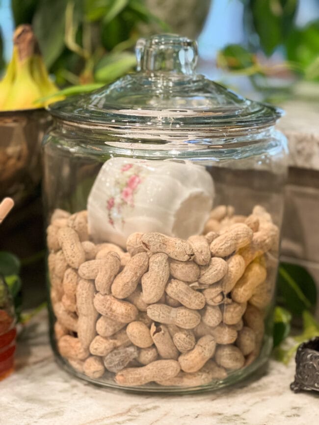 clear jar of peanuts in the shells with a vintage teacup as a scoop