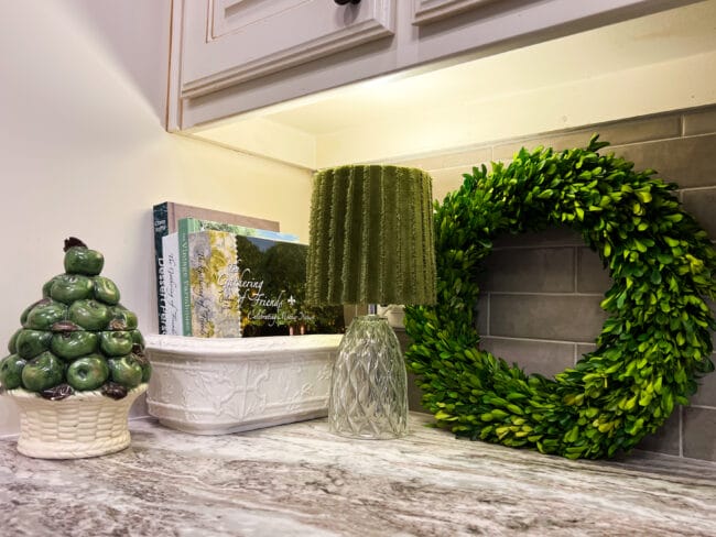 kitchen corner with lamp, wreath, cookbooks and a green apple canister