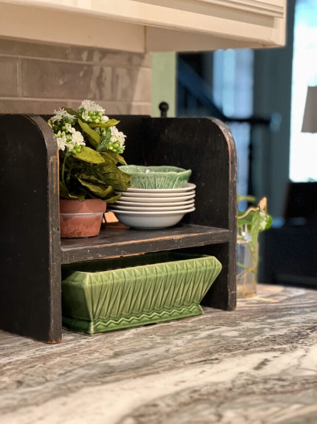 small vintage childs seat used as a shelf on a kitchen counter. Holds small bowls, a plant and green pottery dish underneath