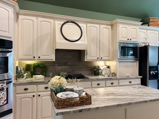 white kitchen cabinets with green ceiling, a round black frame over cooktop and a basket of dishes on kitchen island