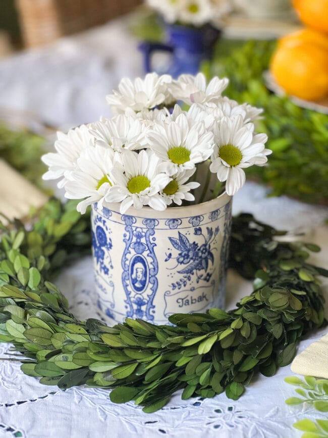 blue and white vintage tobacco jar with white daisies and sitting inside a boxwood wreath