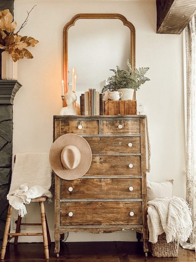 chest of drawers with a mirror above leaning on wall, books, bust and a plant sitting on top