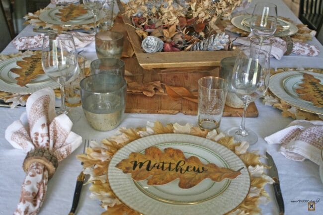 fall tablescape with plates, leaf place cards and leaves in the centerpiece
