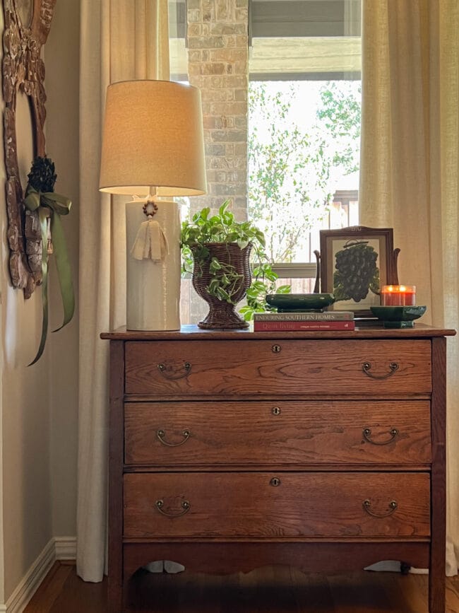 antique chest of drawers with a lamp, plant, books and a candle