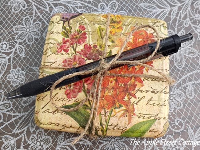 repurposed ear plug case with floral paper and a pen tied together