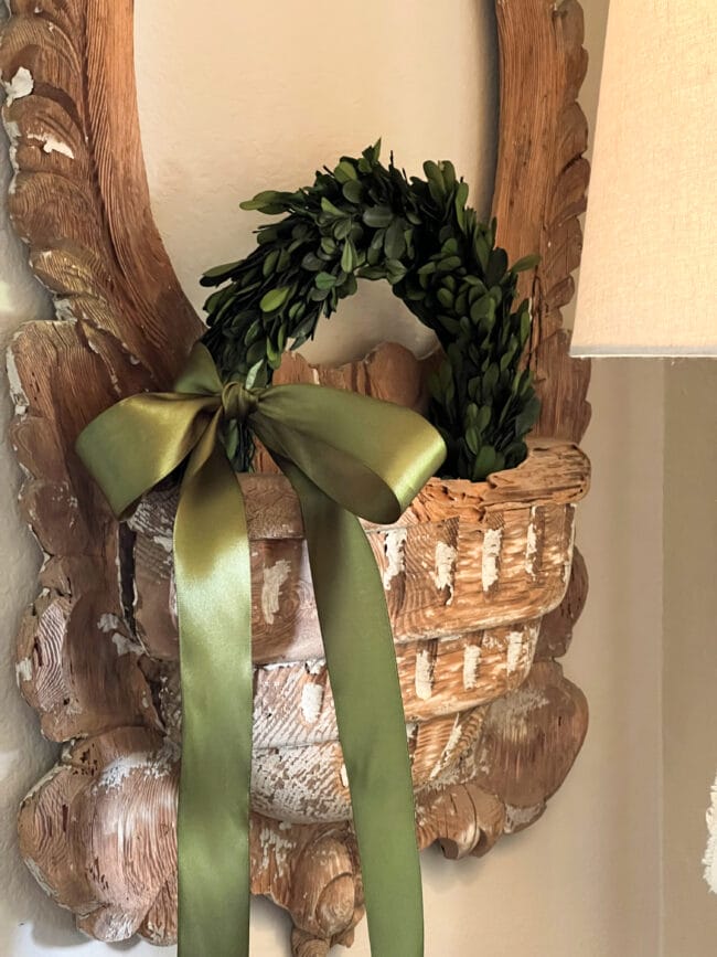 boxwood wreath with green satin bow sitting inside the pocket of an old French mirror