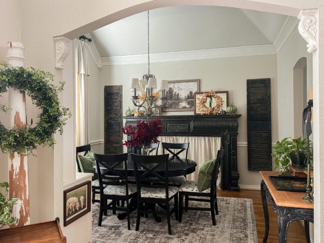 dining room with black mantel, dining table, shutters and decorated with fall leaves, pillows and painting over mantel