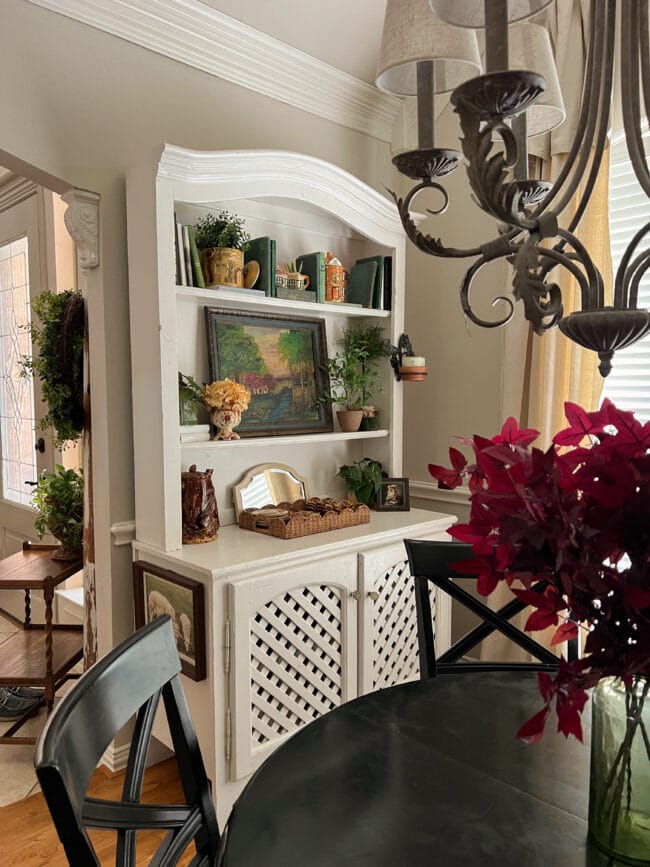 view of faux burgundy leaves in foreground with white dining hutch and fall decor in background