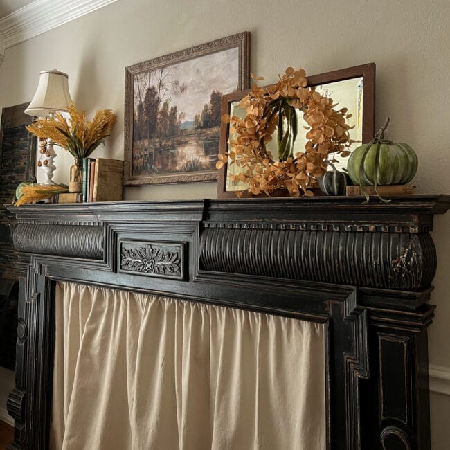 black mantel with fall painting, wreath, mirror, stems and green pumpkins
