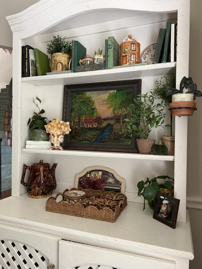 top of hutch with fall painting, books, pottery and plants
