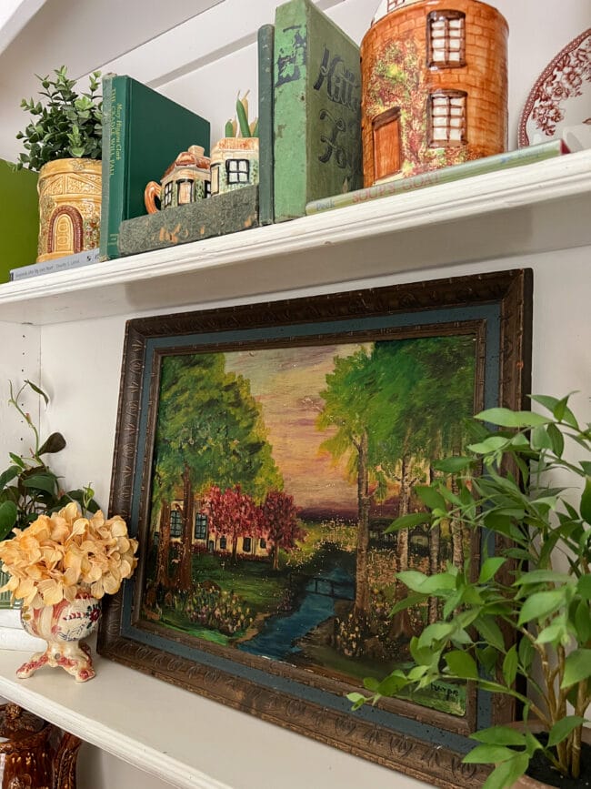 close up of fall colored landscape painting, vintage biscuit jars, green books and plants