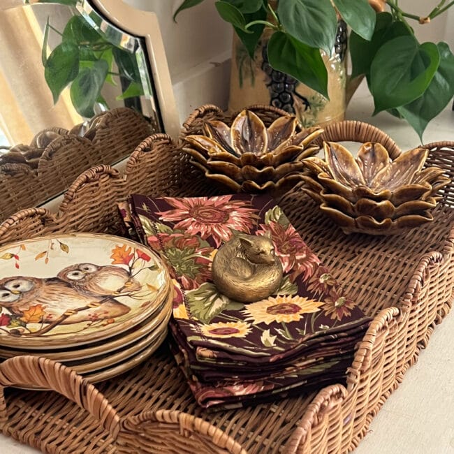 scalloped wicker tray holding fall plates with owls, small gold flower shaped bowls and fall printed napkins with a tiny fox sitting on top